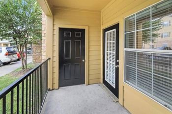 a porch with a black door and a yellow house next to it